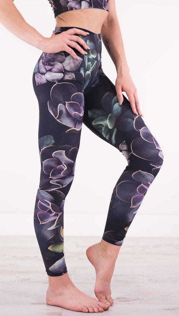 Right view of model wearing black athleisure leggings with green and purple succulent plants throughout