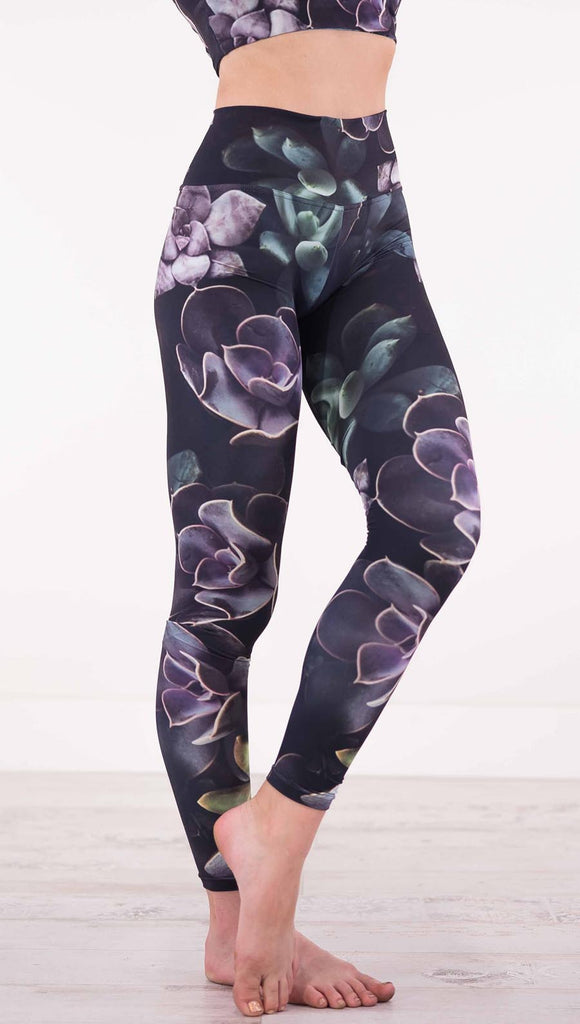 Enhanced right view of model wearing black athleisure leggings with green and purple succulent plants throughout