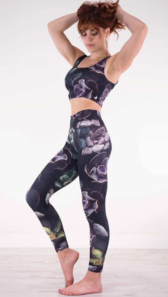 Left view of model wearing black athleisure leggings with green and purple succulent plants throughout