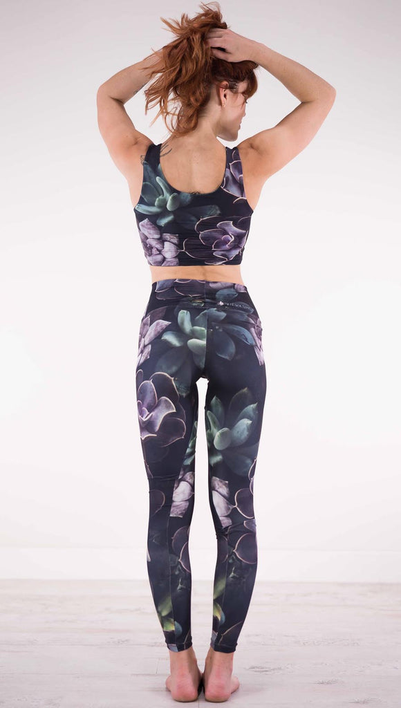 Back view of model wearing black athleisure leggings with green and purple succulent plants throughout