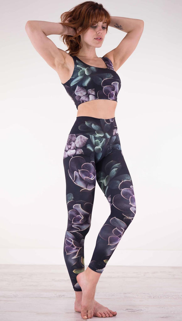 Front view of model wearing black athleisure leggings with green and purple succulent plants throughout