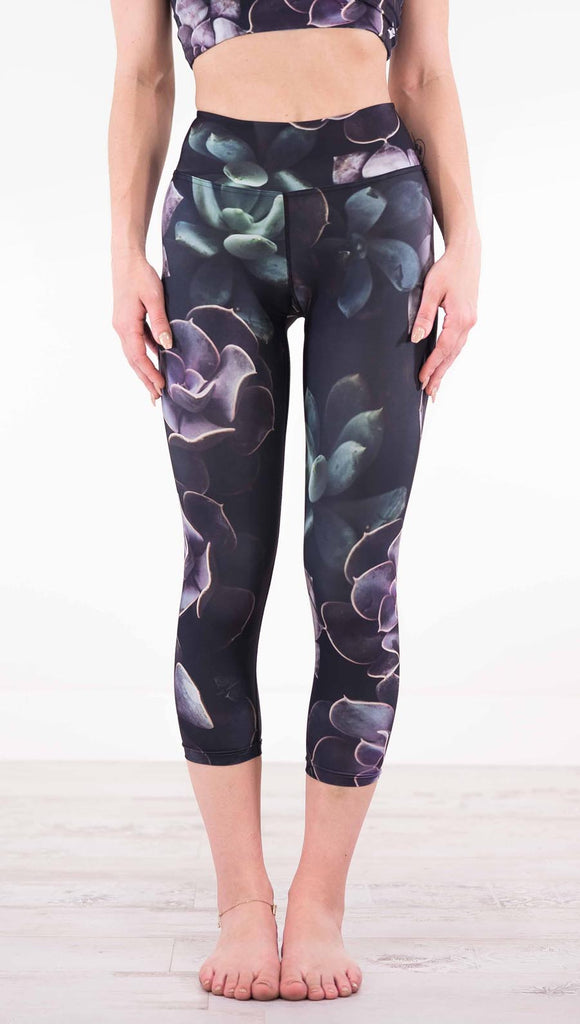 Enhanced front view of model wearing black capri leggings with green and purple succulent plants throughout