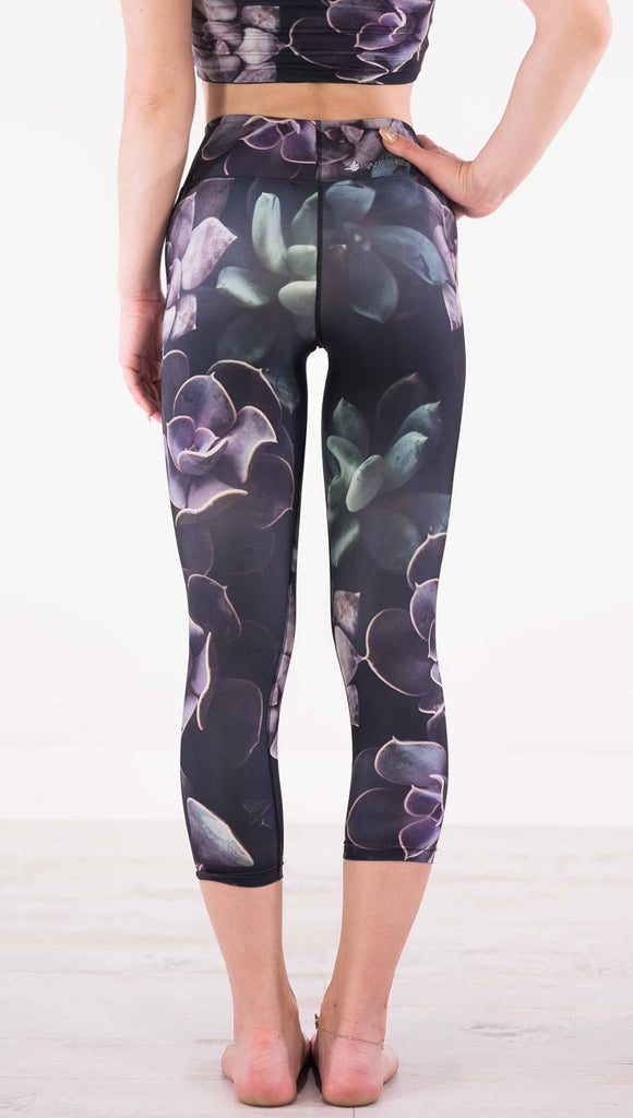 Back view of model wearing black capri leggings with green and purple succulent plants throughout