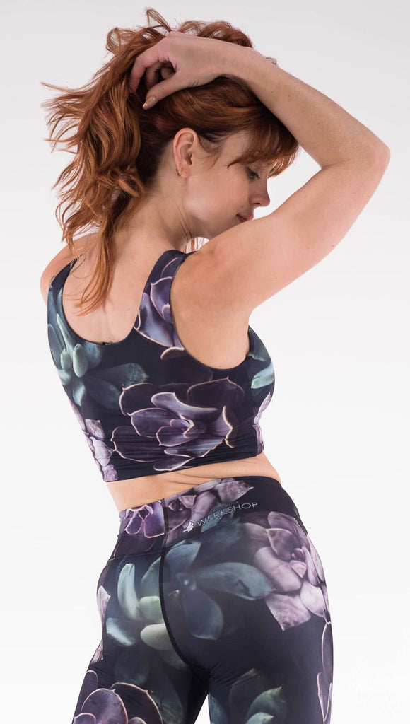 Back view of model wearing the Midnight Garden reversible top. This is in the Midnight Garden side, it is a black crop top with green and purple succulent plants throughout