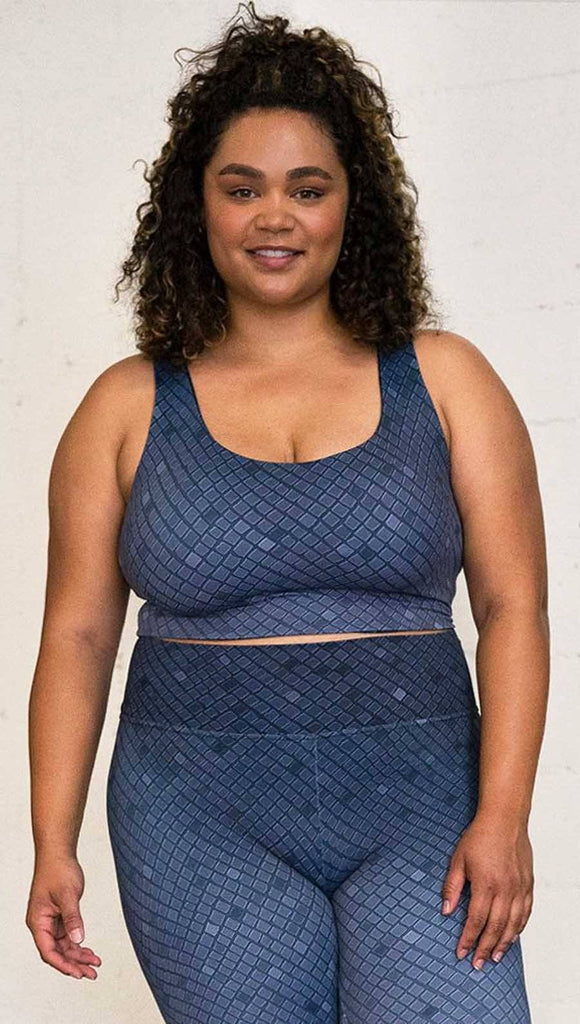 Three quarter length front view of a model wearing a blue mosaic tile print reversible crop top with dark gray mosaic tile print on the other side 