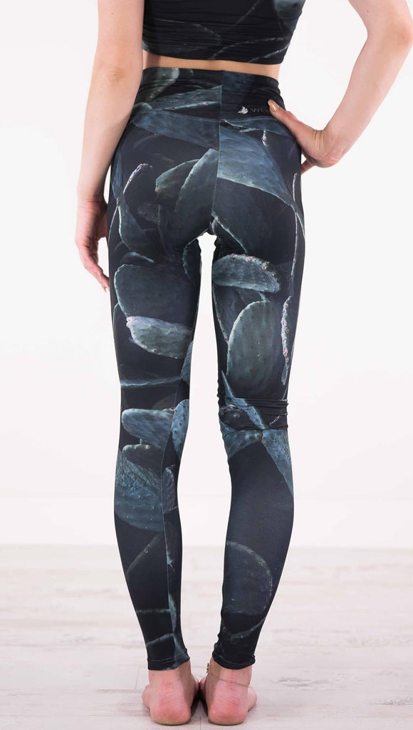 Back view of model wearing black athleisure leggings with dark green cacti plants throughout