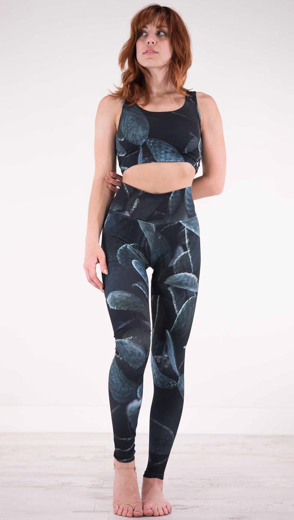 Front view of model wearing black athleisure leggings with dark green cacti plants throughout