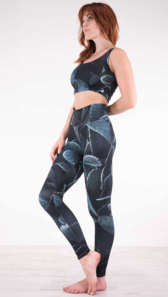 Left view of model wearing black athleisure leggings with dark green cacti plants throughout