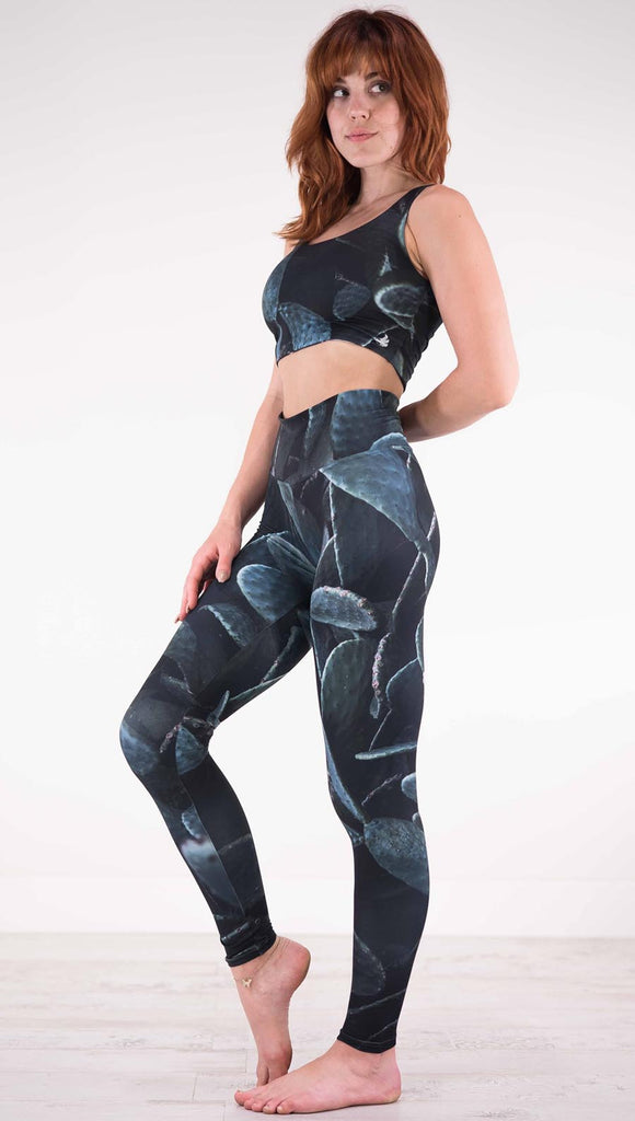 Left view of model wearing black athleisure leggings with dark green cacti plants throughout