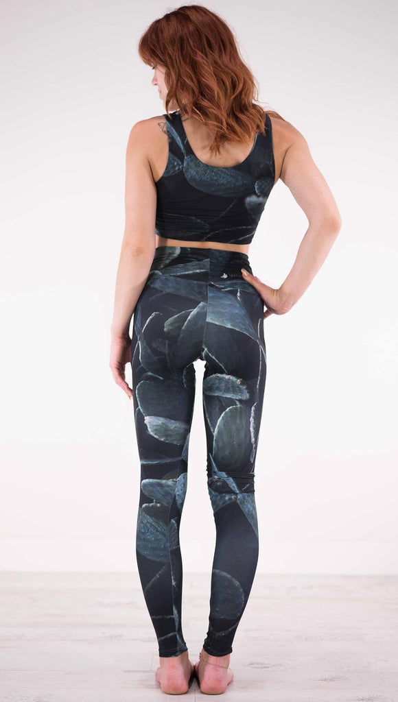 Back view of model wearing black athleisure leggings with dark green cacti plants throughout