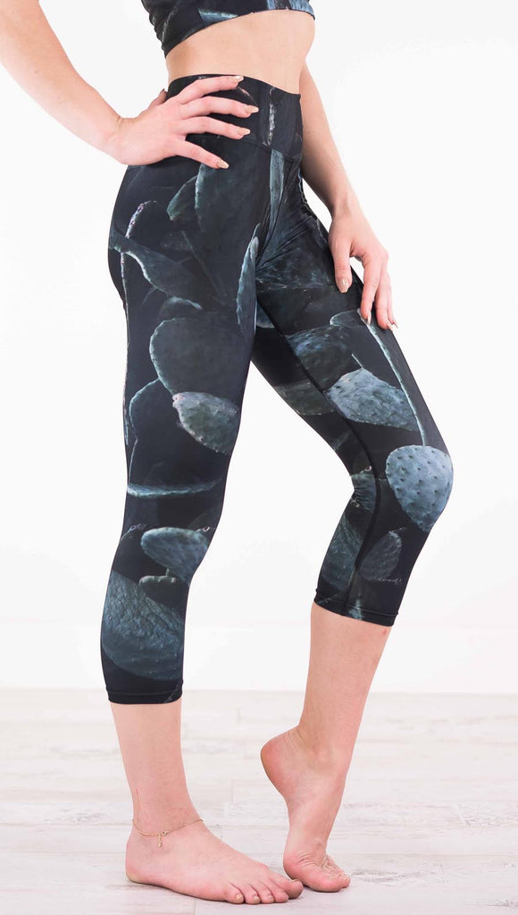 Right view of model wearing black capri leggings with dark green cacti plants throughout