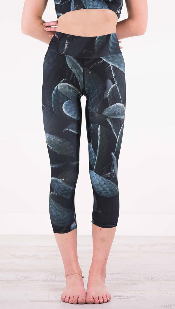 Front view of model wearing black capri leggings with dark green cacti plants throughout