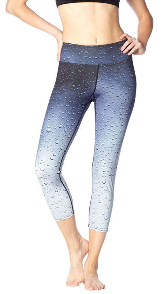 Model wearing WERKSHOP Rain Triathlon Capri Leggings. The leggings are printed with a blue/gray ombre and waterdrops throughout. It goes from dark at the waistband to light and the leg opening.