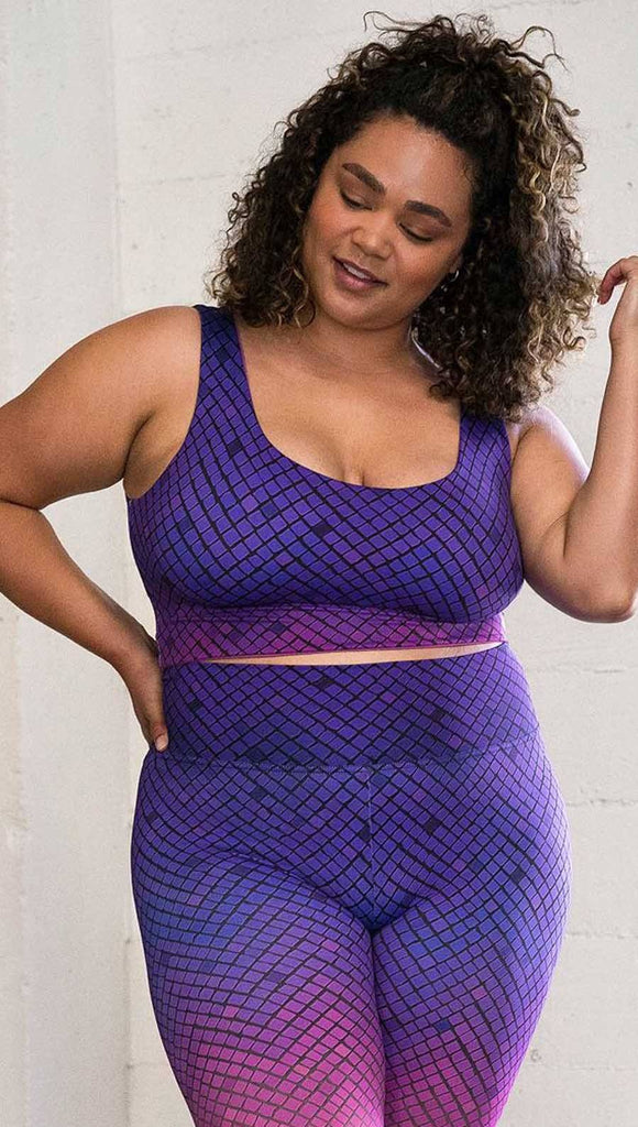 Three quarter length front view of model wearing a reversible crop top with a purple mosaic print on one side and solid fuschia with a small Eagle Rock Werkshop logo on the other side. 