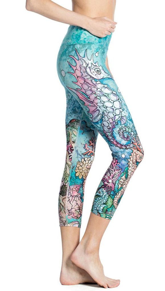 close up right side view of model wearing seahorse and coral reef themed printed capri leggings