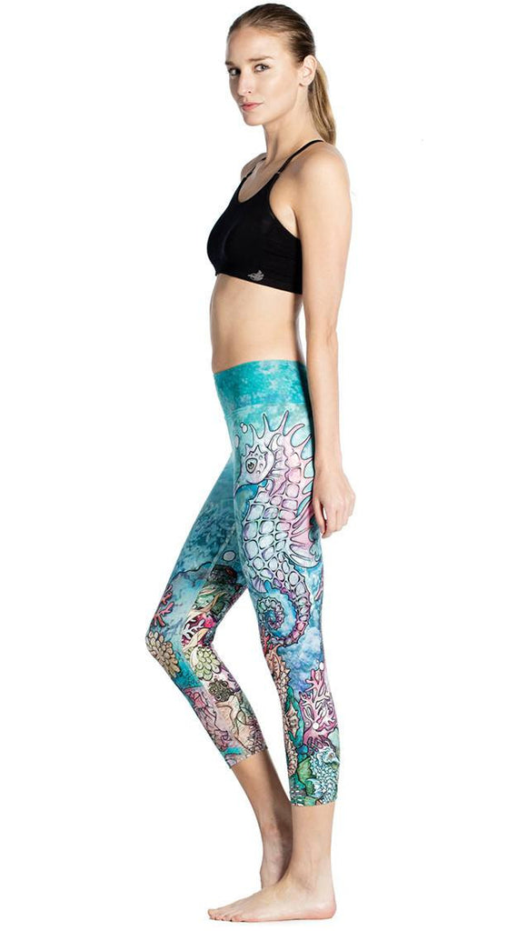 left side view of model wearing seahorse and coral reef themed printed capri leggings