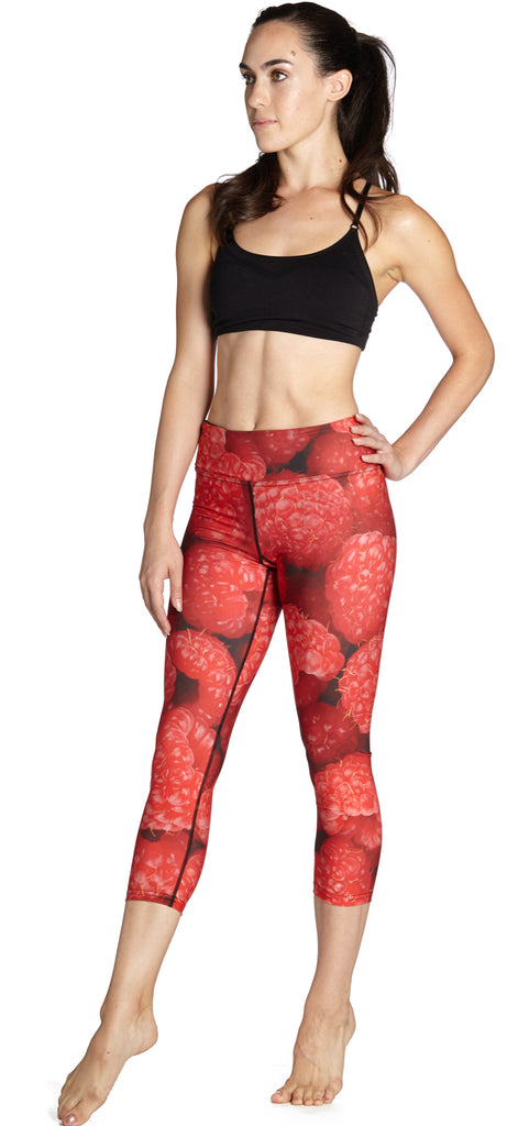 Model wearing WERKSHOP Raspberries Capri Leggings. The leggings are printed with a macro image of raspberries. They are bright red.