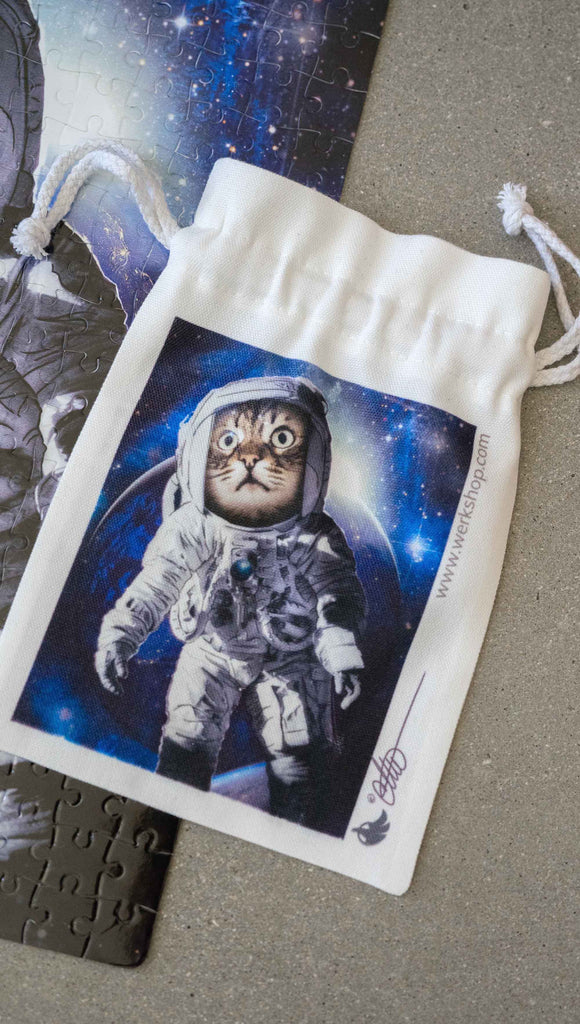 WERKSHOP Space Cat (Catstronaut) canvas drawstring pouch (comes free with matching puzzle)! The artwork features a house cat wearing an astronaut uniform, floating in outer space with a nebula behind him.