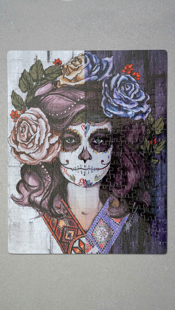 WERKSHOP Sugar Skull Mashup Puzzle. The artwork celebrates Dia De Los Muertos with a drawing of a girl wearing sugarskull makeup surrounded by a wreath of roses.