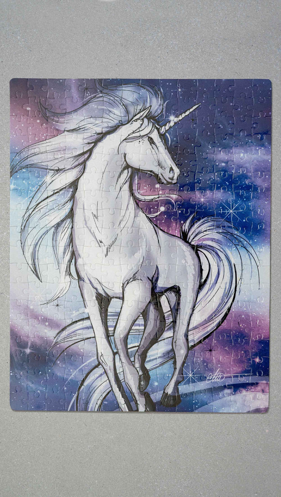 WERKSHOP Unicorn 252 piece jigsaw puzzle. The puzzle is printed with original artwork of a Unicorn by Chriztina Marie. It features a white unicorn prancing on a fantastical galactic background with swirls of purple and blue with sparkles. 