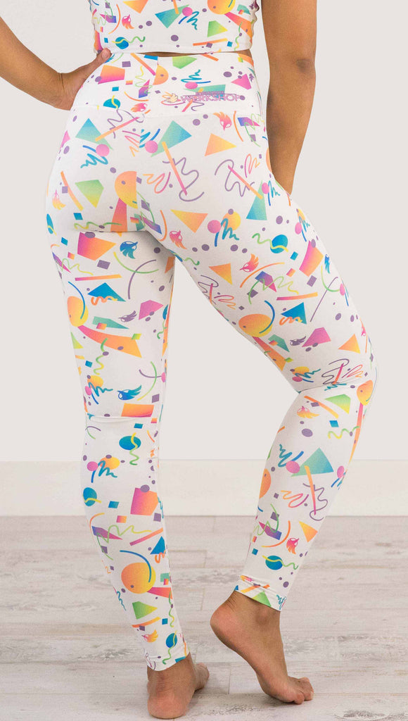 Waist down view of model wearing WERKSHOP white confetti athleisure leggings. The artwork on the leggings shows multi-colored circles, scribbles and triangles over a white background.