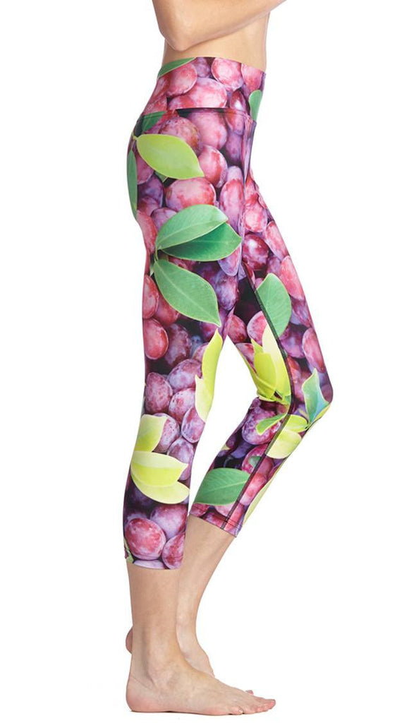 close up right side view of model wearing grapes and leaves themed printed capri leggings