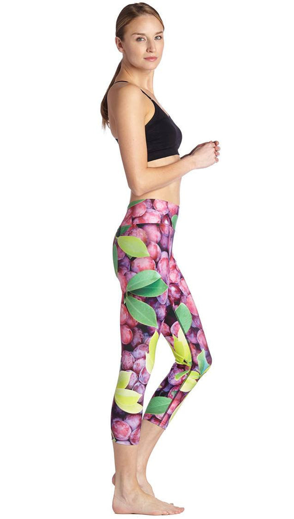 right side view of model wearing grapes and leaves themed printed capri leggings