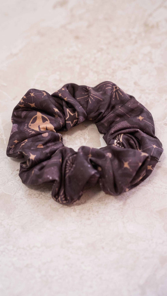 Zodiac theme printed hair scrunchie with zodiac themed artwork with the sun and moon with the moon phases, shooting stars and all 12 zodiac constellations in gold over a dark purple background. 